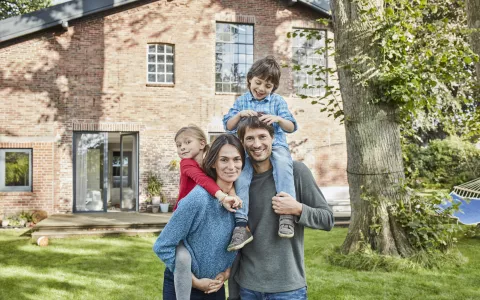 Eltern mit Kindern fröhlich im Garten vor ihrem Haus